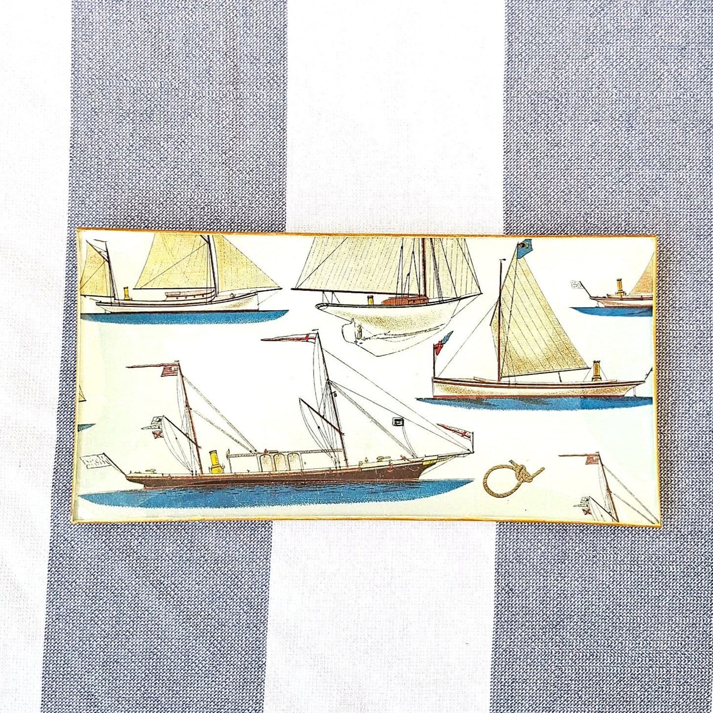 Bandejas decorada a mano con estampado náutico de veleros sobre fondo beige. El diseño presenta una variedad de embarcaciones de vela en tonos beige, marrón y azul, incluyendo veleros clásicos, barcos de pesca tradicionales y yates con diferentes tipos de velas. El patrón incluye también elementos marinos como anclas, nudos marineros y pequeños detalles náuticos distribuidos entre las embarcaciones. Las bandejas tienen bordes con ribete dorado. Artesanía española Dmarta