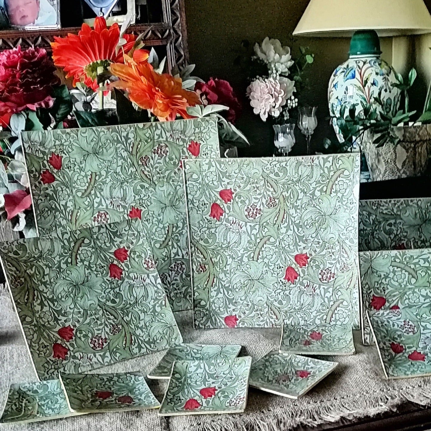 Conjunto de platos y bandejas en cristal decorado a mano en España. El estampado es de William Morris "Golden lily" en tonos tierra con hojas verdes entrelazadas, flores rojas y detalles dorados sobre fondo beige. Diseño Arts and Crafts con motivos florales estilizados y volutas ornamentales."
