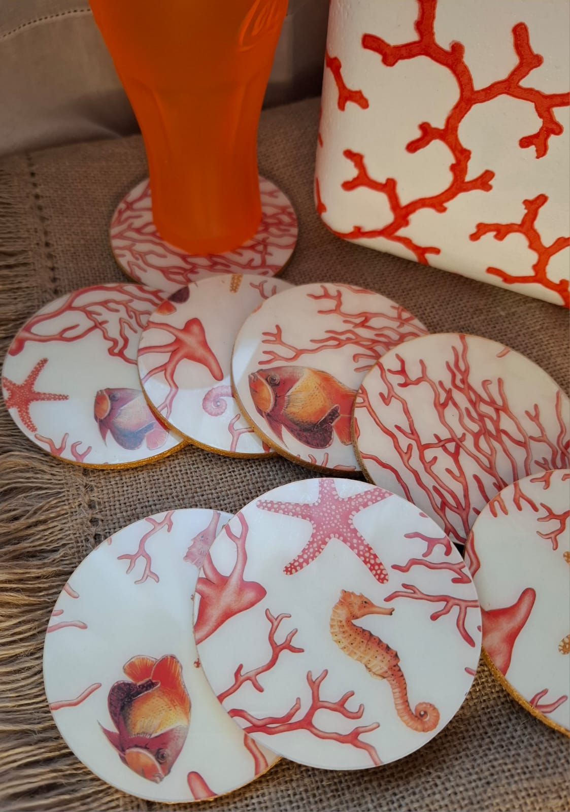 Posavasos realizados a mano po Dmarta con base de corcho y decorados con estampado de corales, peces, estrellas y caballitos de mar. Los colores van en la gama de lo corales y naranjas sobre fondo blanco. Los bordes acabados en color dorado le dan un toque elegante y único. Artesanía Española.