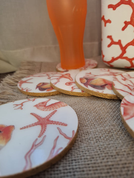 Posavasos realizados a mano po Dmarta con base de corcho y decorados con estampado de corales, peces, estrellas y caballitos de mar. Los colores van en la gama de lo corales y naranjas sobre fondo blanco. Los bordes acabados en color dorado le dan un toque elegante y único. Artesanía Española.