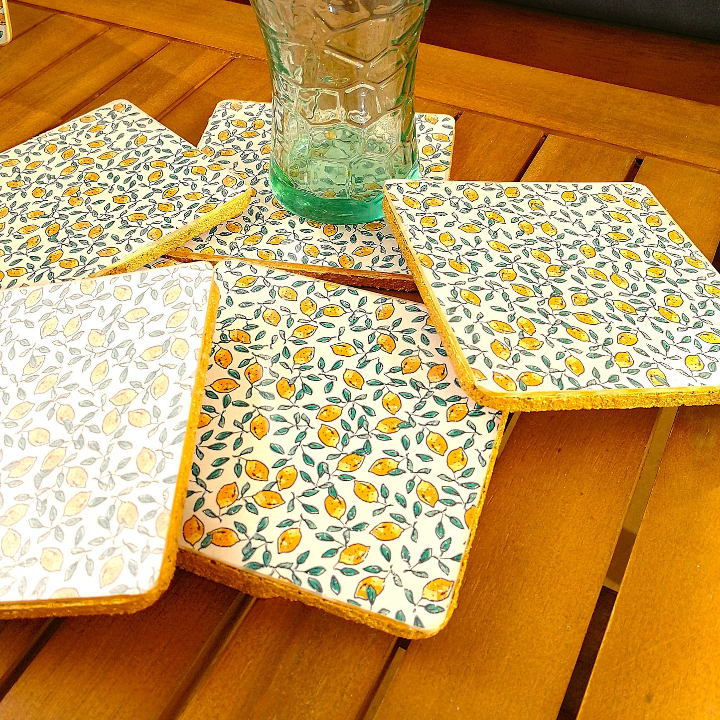 Detalle posavasos realizados a mano con decoupàge. Son cuadrados con bordes redondeados y tienen una base de corcho, ideal para proteger superficies del calor y la humedad. Estampado de limones con hojas verdes sobre fondo blanco. El patrón es pequeño y repetitivo, lo que le da un aire fresco, veraniego y mediterráneo. Transmiten sensación de frescura, ideal para disfrutar bebidas frías en días soleados.