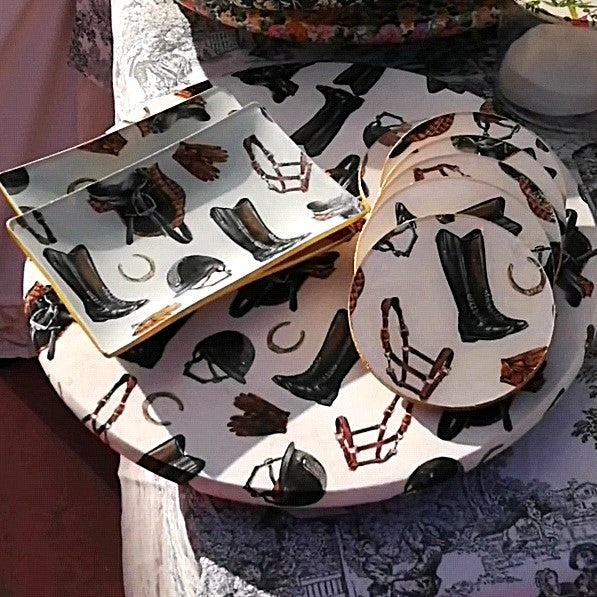 "Bandeja redonda, bandejas y posavasos con estampado ecuestre sobre fondo blanco con motivos de botas de montar negras y marrones, cascos, herraduras y elementos de equitación. Diseño temático hípico ideal para servir aperitivos o como elemento decorativo."
