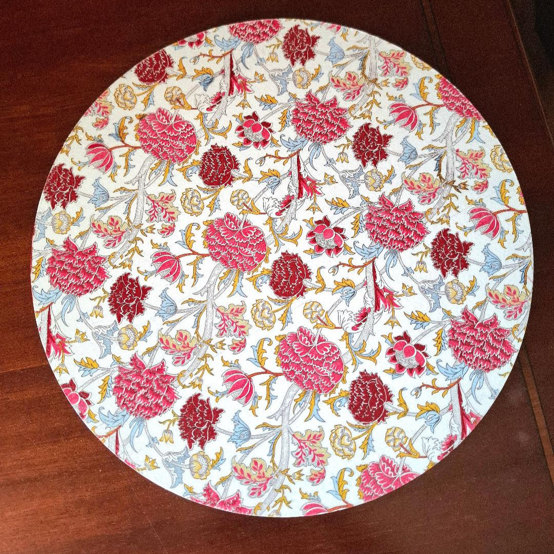 "Tabla giratoria artesanal con estampado floral de claveles en tonos rojos, rosas y azules, borde decorado con greca, diseño elegante y atemporal"