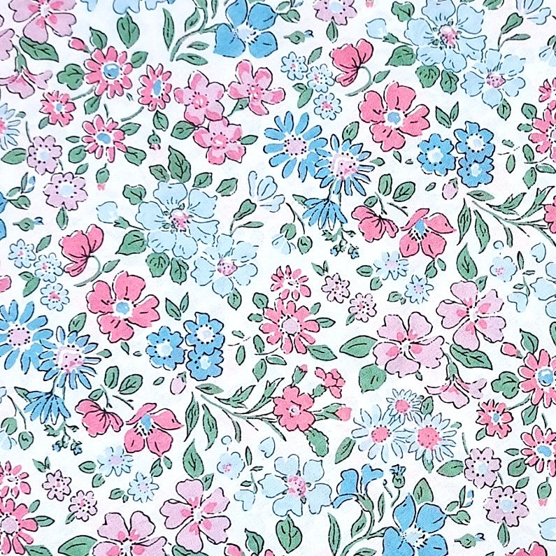 Este diseño específico presenta un delicado patrón floral con flores en diversas tonalidades de rosa y celeste combinadas con verdes suaves en sus hojas. El fondo es blanco, lo que resalta aún más la belleza del estampado.