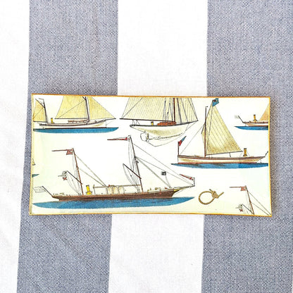 Bandejas decorada a mano con estampado náutico de veleros sobre fondo beige. El diseño presenta una variedad de embarcaciones de vela en tonos beige, marrón y azul, incluyendo veleros clásicos, barcos de pesca tradicionales y yates con diferentes tipos de velas. El patrón incluye también elementos marinos como anclas, nudos marineros y pequeños detalles náuticos distribuidos entre las embarcaciones. Las bandejas tienen bordes con ribete dorado. Artesanía española Dmarta