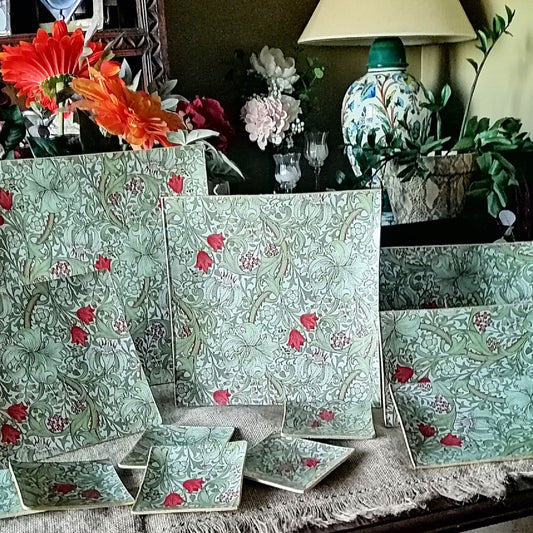 Conjunto de platos y bandejas en cristal decorado a mano en España. El estampado es de William Morris "Golden lily" en tonos tierra con hojas verdes entrelazadas, flores rojas y detalles dorados sobre fondo beige. Diseño Arts and Crafts con motivos florales estilizados y volutas ornamentales."