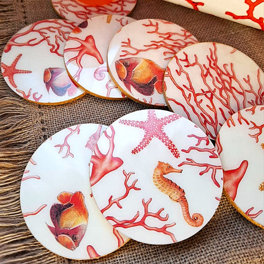 Posavasos realizados a mano po Dmarta con base de corcho y decorados con estampado de corales, peces, estrellas y caballitos de mar. Los colores van en la gama de lo corales y naranjas sobre fondo blanco. Los bordes acabados en color dorado le dan un toque elegante y único. Artesanía Española.