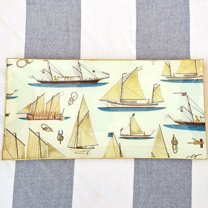 Bandejas decorada a mano con estampado náutico de veleros sobre fondo beige. El diseño presenta una variedad de embarcaciones de vela en tonos beige, marrón y azul, incluyendo veleros clásicos, barcos de pesca tradicionales y yates con diferentes tipos de velas. El patrón incluye también elementos marinos como anclas, nudos marineros y pequeños detalles náuticos distribuidos entre las embarcaciones. Las bandejas tienen bordes con ribete dorado. Artesanía española Dmarta