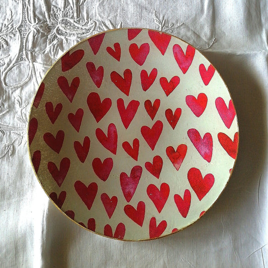 Plato de cristal decorado a mano con  estampado de corazones rojos en distintas formas y tamaños, distribuidos de forma irregular sobre un fondo blanco. Los corazones tienen un acabado algo texturizado, con variaciones sutiles de tono y sombreados que les dan un aire hecho a mano. 
Es ideal para decoración de San Valentín o detalles amorosos con un toque artesanal y alegre.