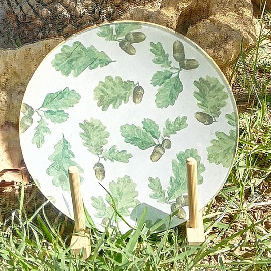 Plato de cristal decorado a mano con estampado con hojas de roble en distintos tonos de verde y pequeñas bellotas marrones que aportan calidez y contraste. El fondo blanco resalta la frescura del verde y mantiene el diseño limpio y ligero. Ideal para decorar mesas rústicas, ambientes naturales o como regalo especial.