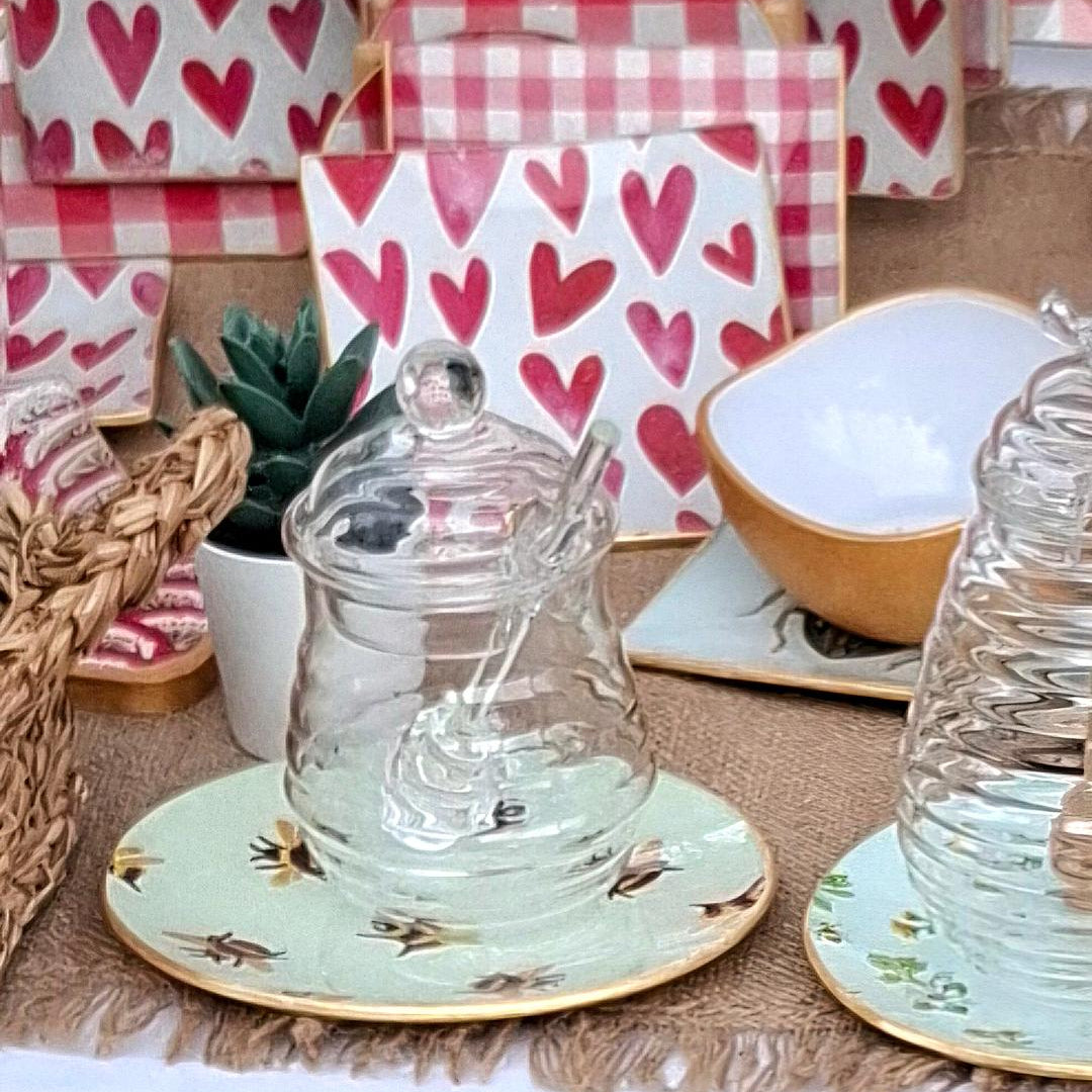 "Composición de mesa con platos decorativos con diseño de abejas sobre fondo azul menta, tarros de cristal y servilletas con corazones rosas y cuadros vichy en ambiente acogedor"