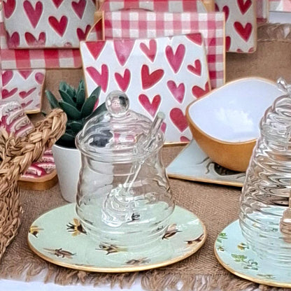 "Composición de mesa con platos decorativos con diseño de abejas sobre fondo azul menta, tarros de cristal y servilletas con corazones rosas y cuadros vichy en ambiente acogedor"