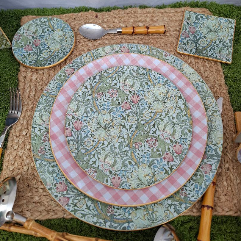 "Vajilla completa con diseño floral verde y rosa estilo William Morris combinada con plato de cuadros vichy rosa, presentada sobre mantel individual de yute con cubiertos de bambú"