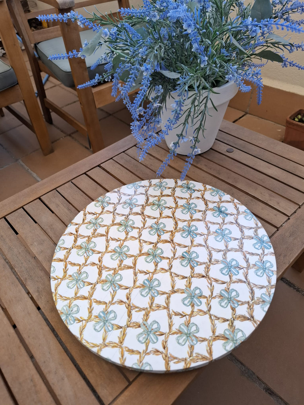 Tabla giratoria Celosía Floral sobre mesa de madera, con flores azul suave y celosía dorada sobre fondo blanco