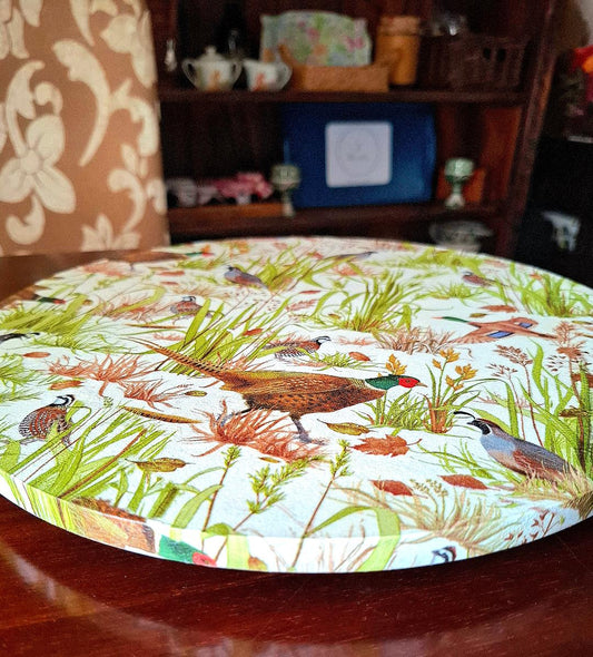 "Tabla giratoria con diseño de faisanes y flora silvestre en tonos verdes, marrones y rojos sobre mesa de madera en ambiente rústico"
