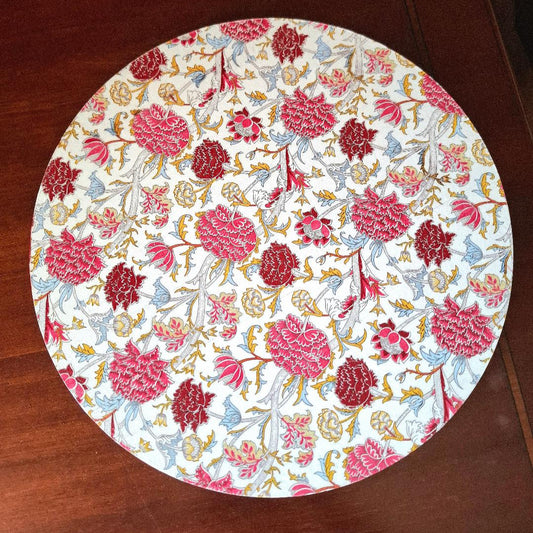 "Tabla giratoria artesanal con estampado floral de claveles en tonos rojos, rosas y azules, borde decorado con greca, diseño elegante y atemporal" 